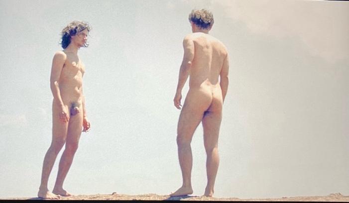 Two naked men standing on a rock

Description automatically generated